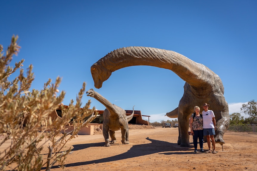 Tourists pose for a photo in front of two huge dinosaur statues.