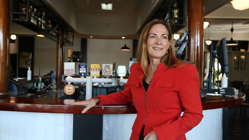 Eumundi CEO Suzanne Jacobi-Lee wears a red jacket and smiles in front of a bar.