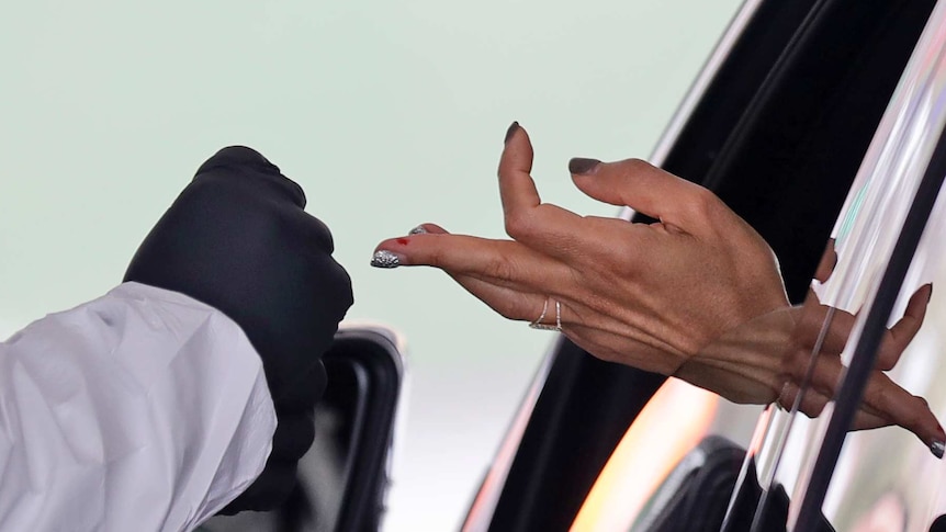 A woman's hand sticks out from a car window, the middle finger with a patch of blood is extended towards a gloved hand.