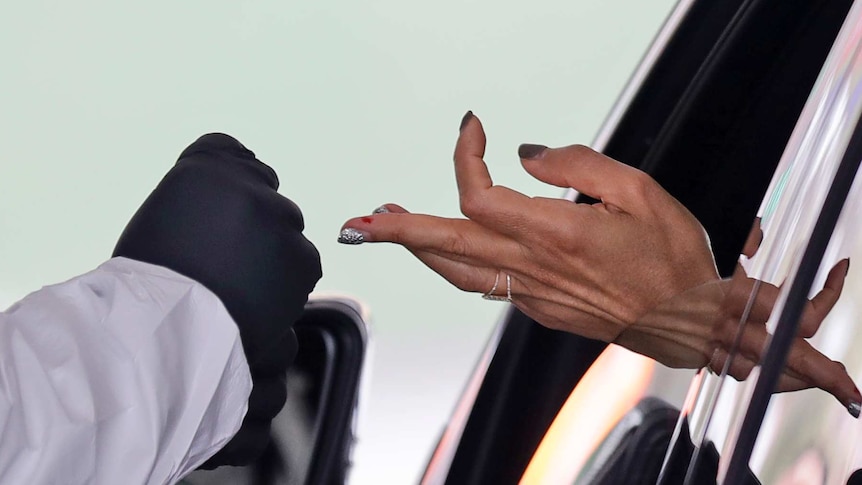 A woman's sticks out from a car window, the middle finger with a patch of blood is extended towards a gloved hand.