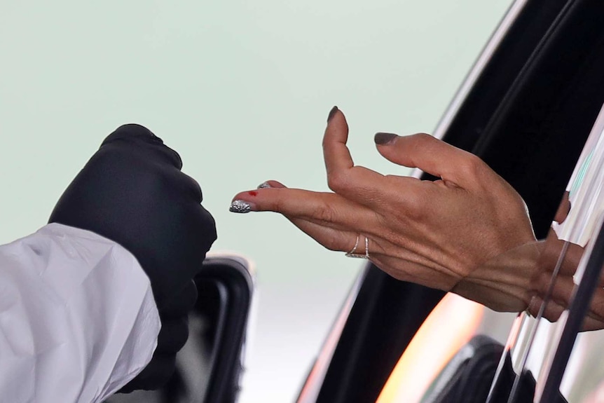 A woman's sticks out from a car window, the middle finger with a patch of blood is extended towards a gloved hand.