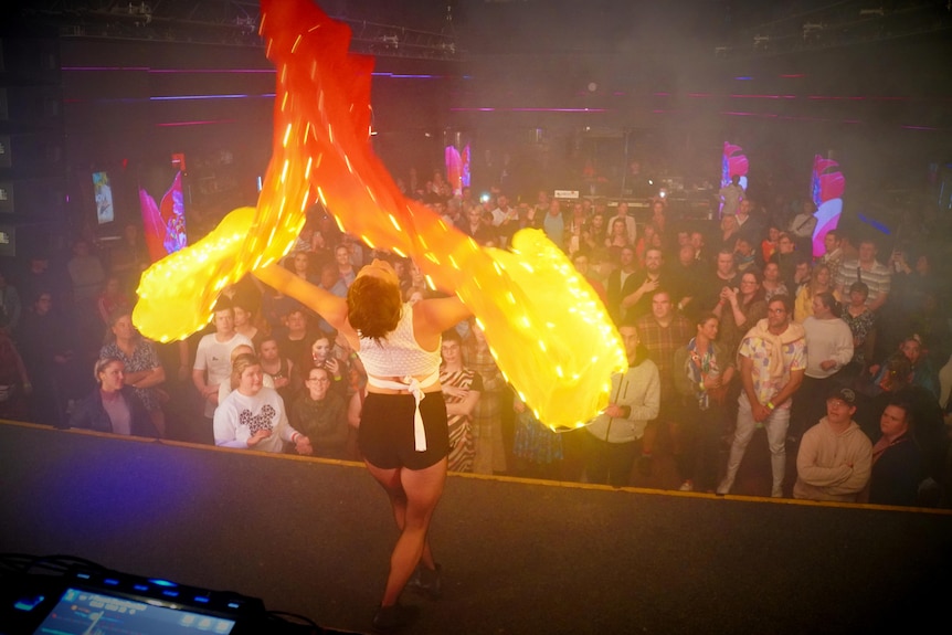 A crowd of onlookers watch a dancer on a stage. 