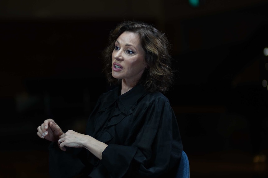 Tina Arena sits in a chair and speaks during a TV interview on a stage.