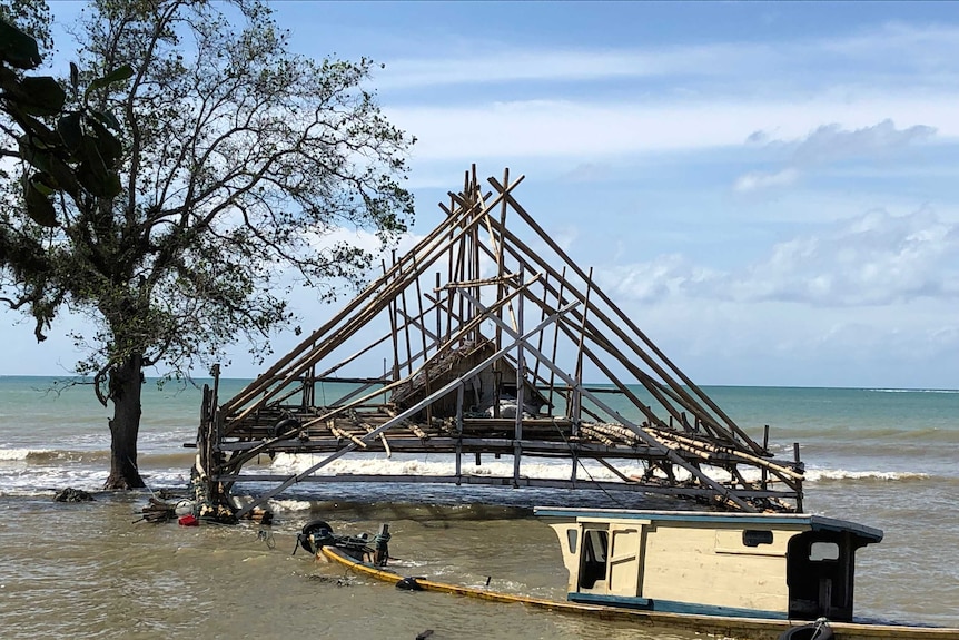 A sunken boat is tied to a pylon in front of an over water shack.