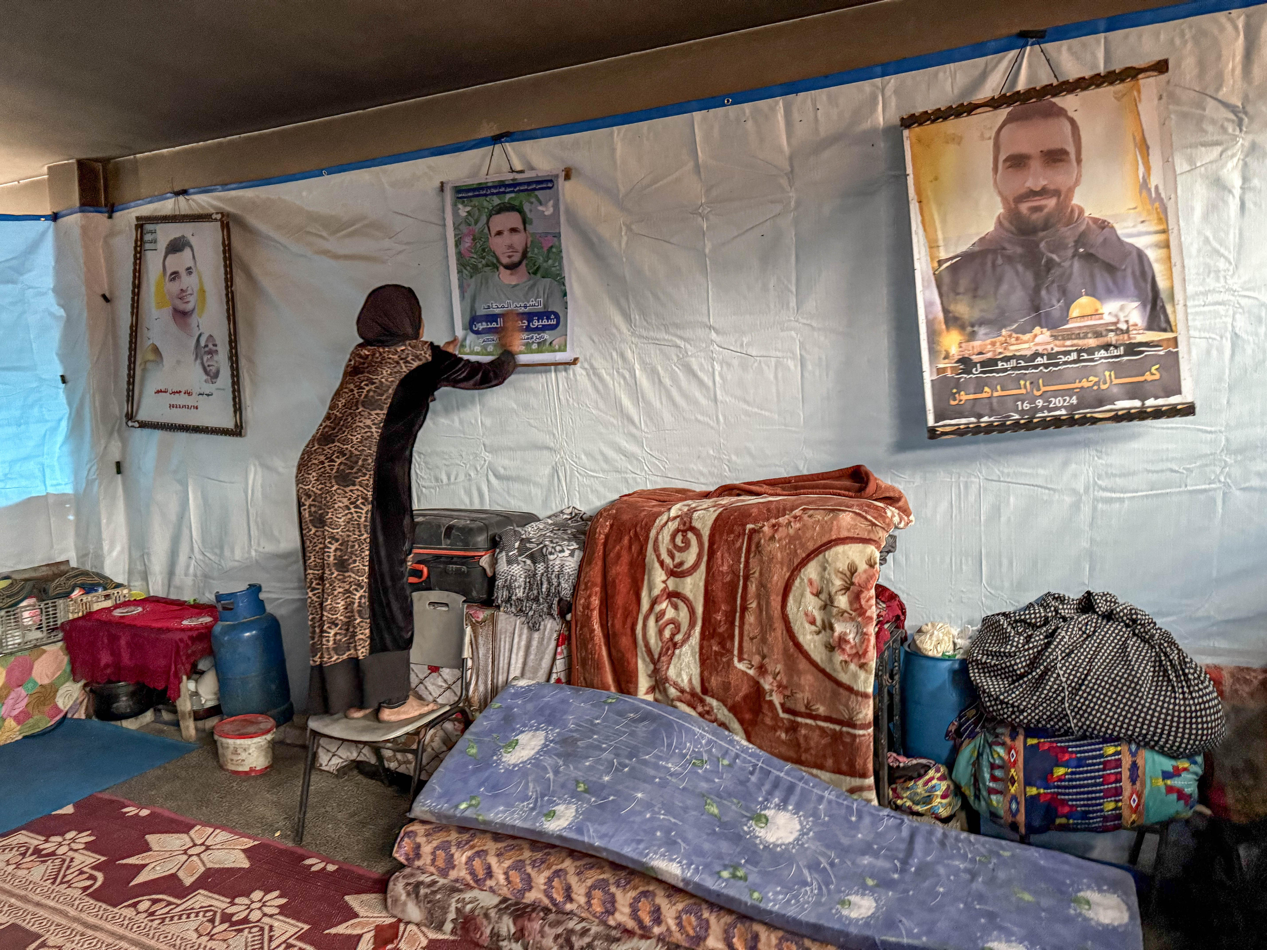 A woman touches a photo of her son which is hanging on a wall. There are also photos of two of her other sons on the wall.
