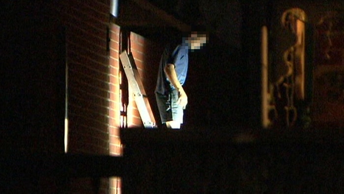 A man walking down a ladder from a roof at night