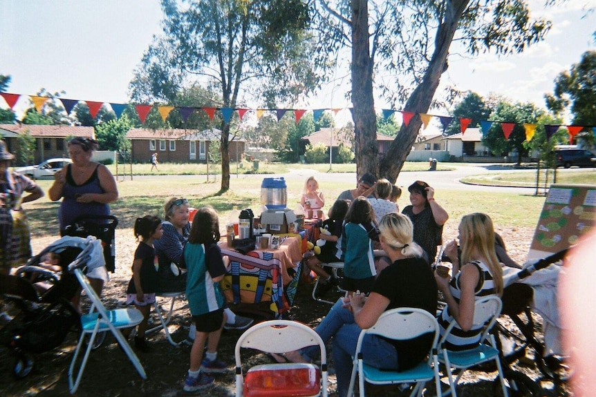 Women and children gather around a table in a park