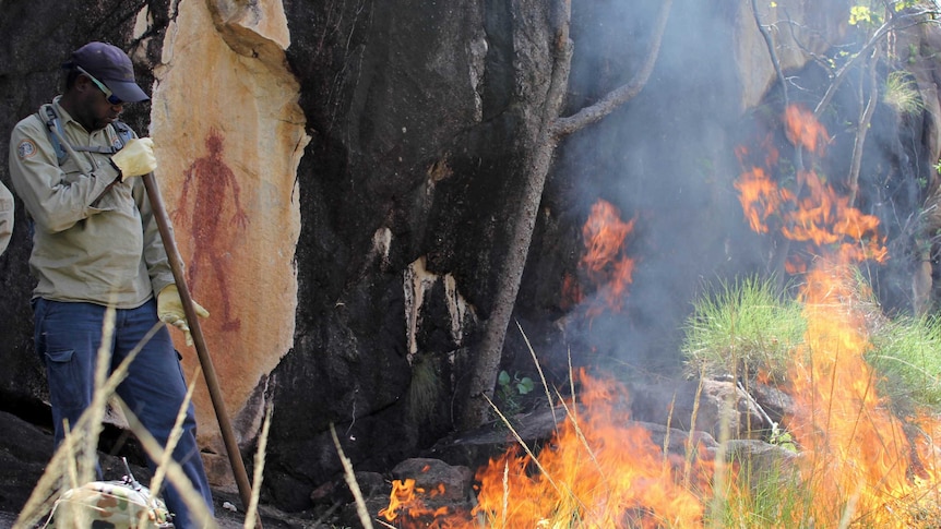 a man tends a grass fire near Indigenous rock art