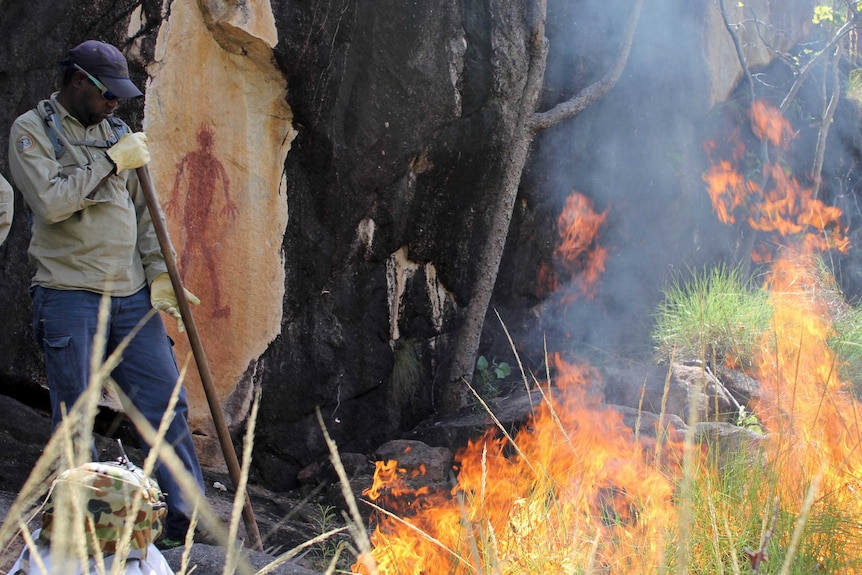 a man tends a grass fire near Indigenous rock art