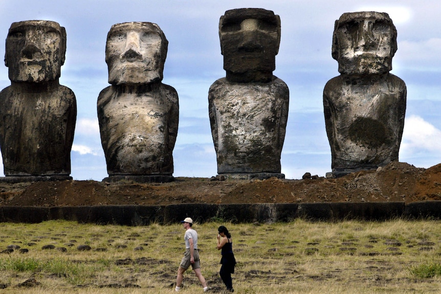 Two tourists walk in front of moai statues.