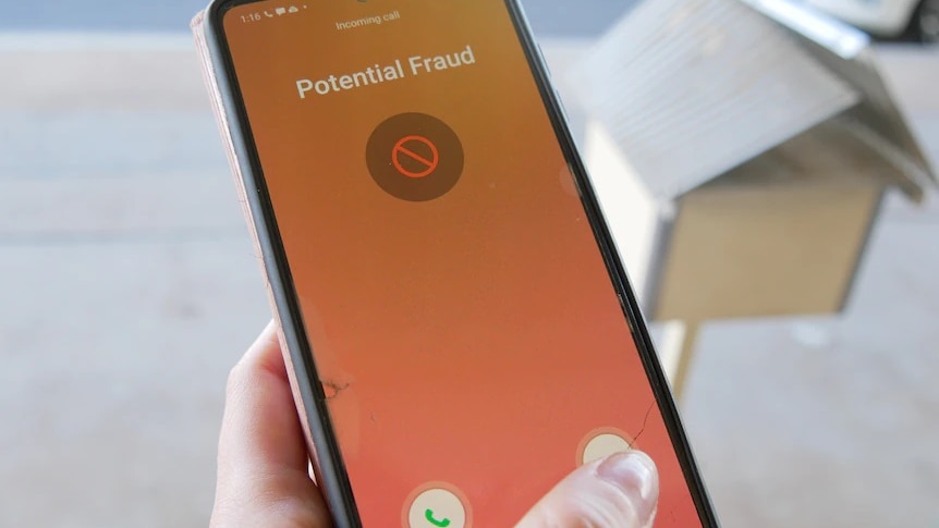 A person holds a mobile phone, the screen showing 'potential fraud' warning message