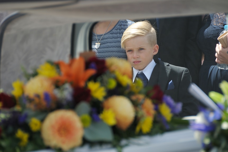 A young boy stands near a coffin.
