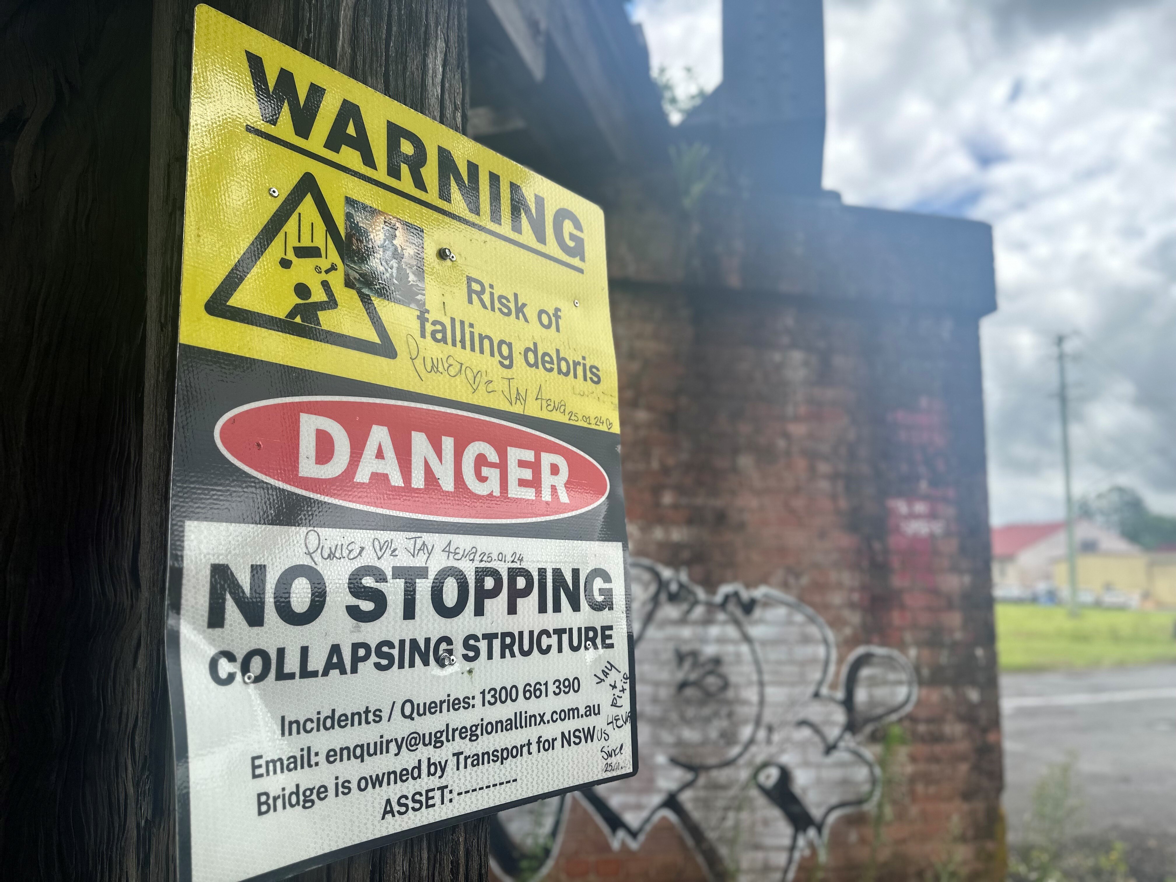 古い鉄道橋からの落下物について歩行者に警告する大きな看板。