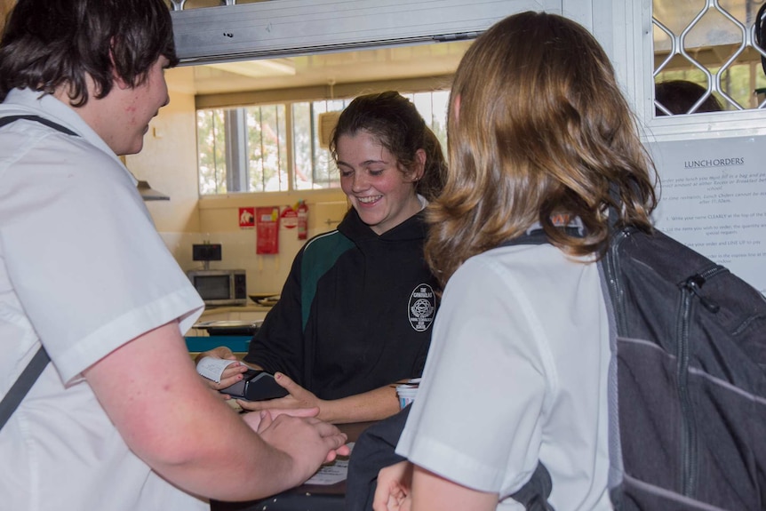 A school student pulls an eftpos receipt from a machine as she serves two other students at a canteen