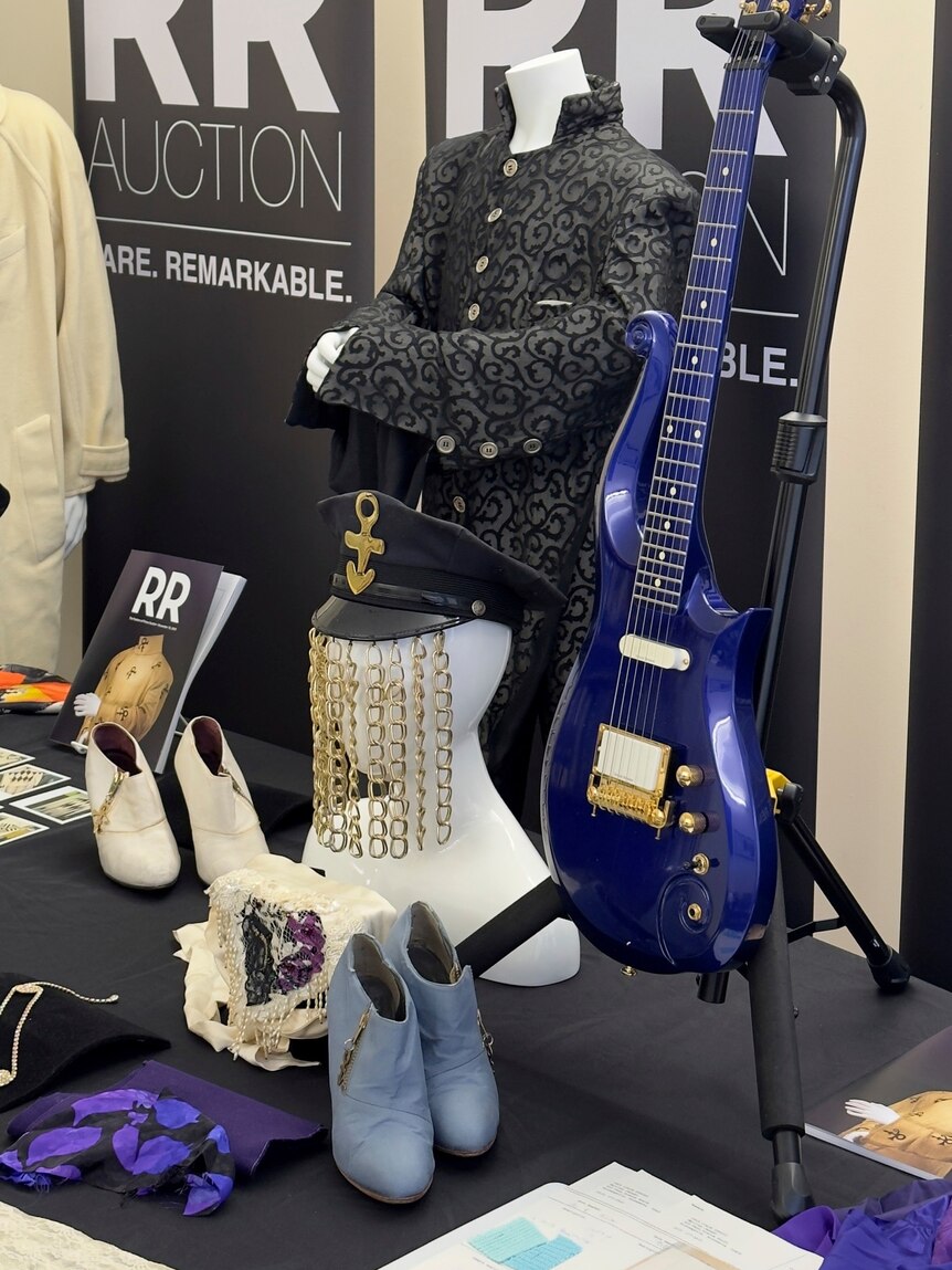 A blue-ish purple guitar stands next to memorabilia.