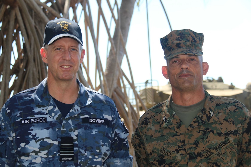 The pair stand in uniform by palm trees