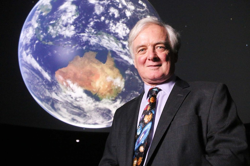 A man stands in front of a globe of planet earth.