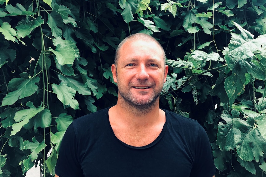 A man wearing a black shirt smiles at the camera.