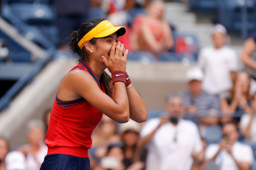 Female tennis player with her hand over her mouth smiling after winning a match