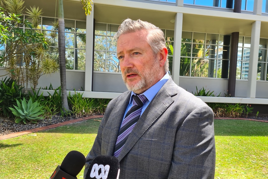 A grey-haired man in a dark suit stands outside speaking to the media.