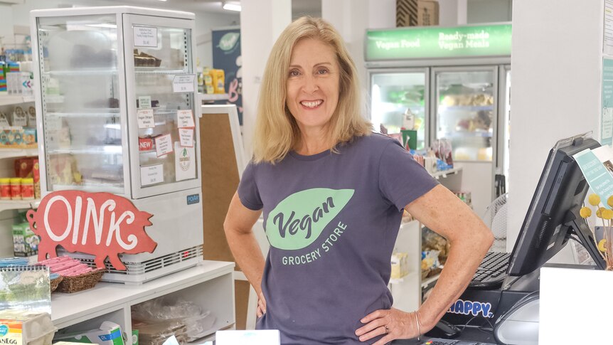Jessica wears a shirt that says Vegan Grocer and stands with her hands on her hips behind a counter loaded with chocolates
