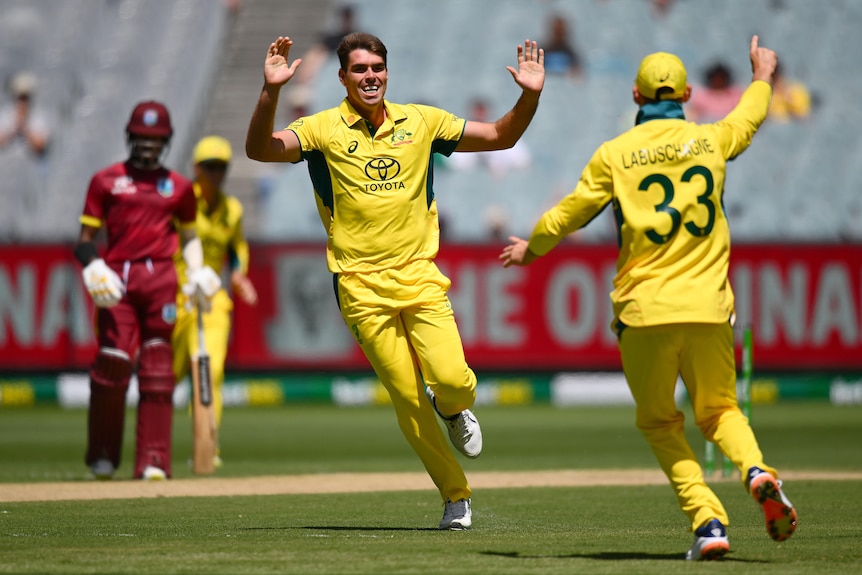 Australian fast bowler Xavier Bartlett grins as he runs toward a teammate with palms out for a high five after a wicket. 