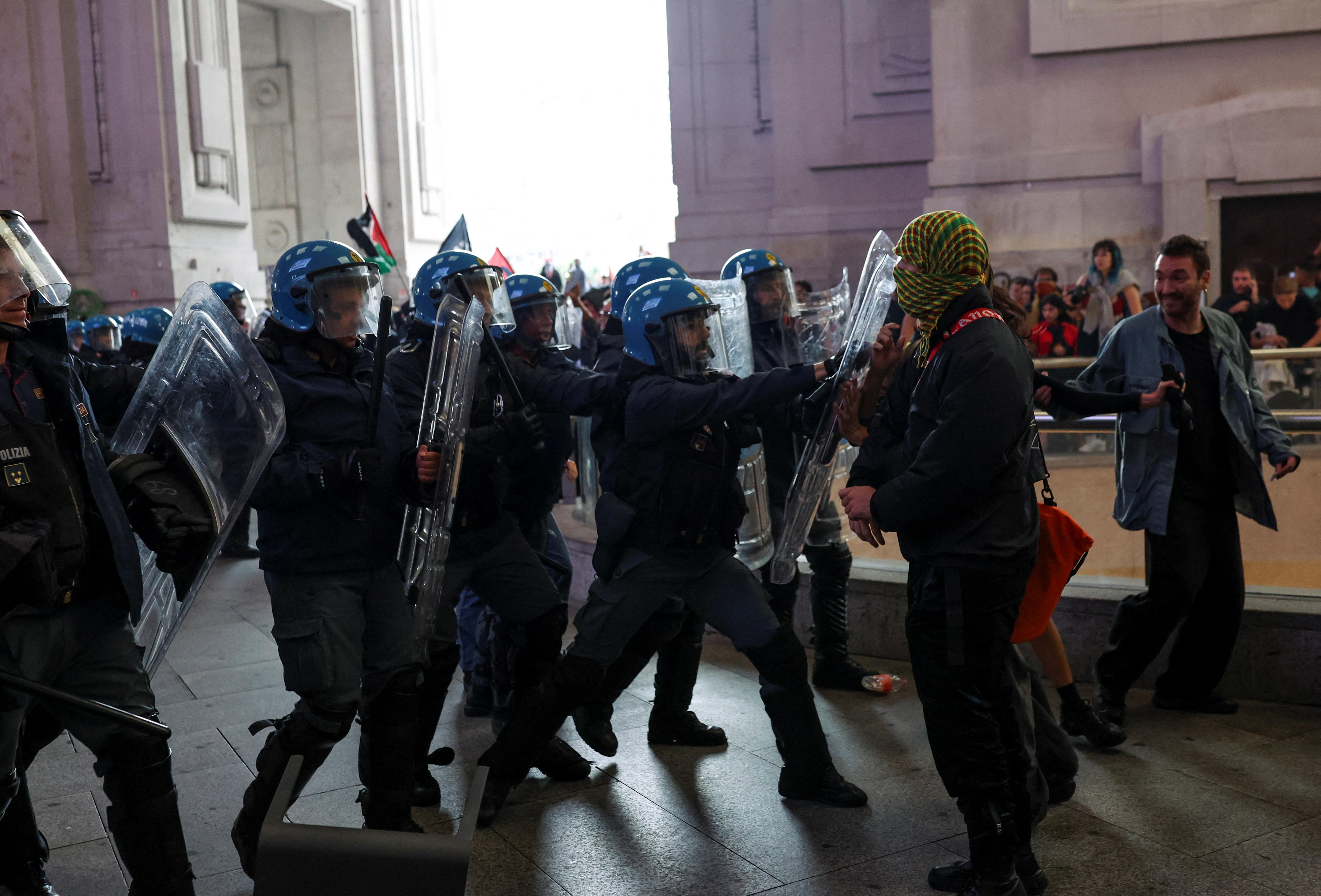 A line of police pushing back a protester inside a large marble entrance to a train station.