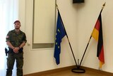 Army officer standing next to German and EU flags.