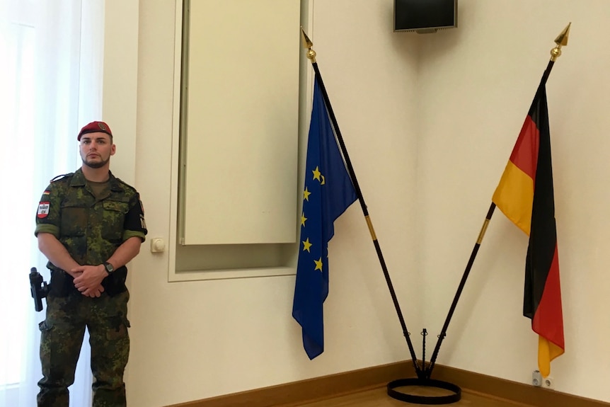 Army officer standing next to German and EU flags.