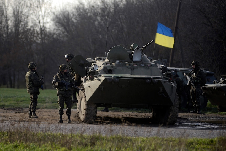 Ukranian troops stand guard at a checkpoint near the city of Izium, with a Ukrainian flag on tank