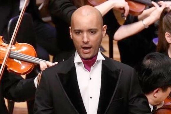 Shanul Sharma, in suit, singing in front of orchestra