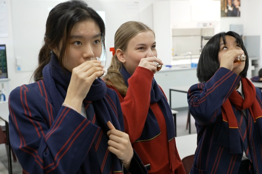 Image: Three school students drinking from small glasses. 