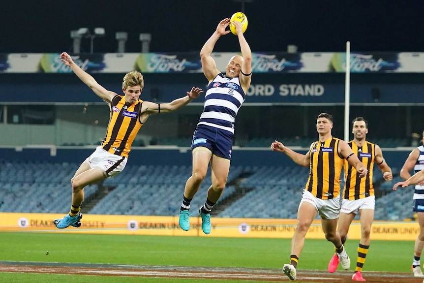 An AFL player extends his arms above his head while mid-air to take a big mark.