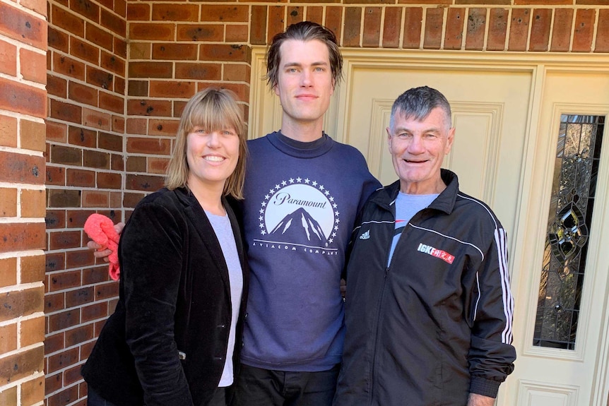 Medium portrait shot of a woman and two men standing outside the front of a house.