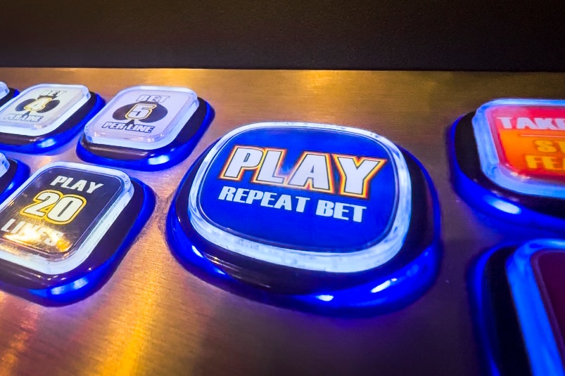 A blue button reads 'PLAY REPEAT BET', on a silver panel of glowing poker machine buttons.