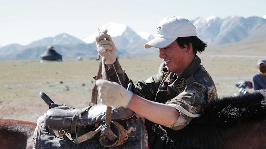 A Mongolian shepherd repairs his saddle