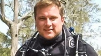 A man in a black wetsuit wearing dive gear.