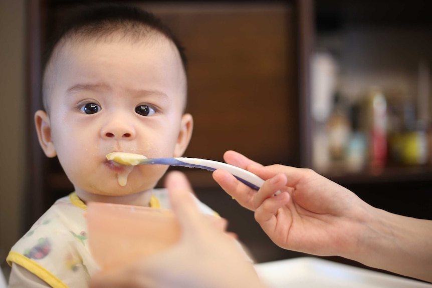 Baby being spoonfed in a story about babies' and kids' food allergies and what to do before changing their diet.