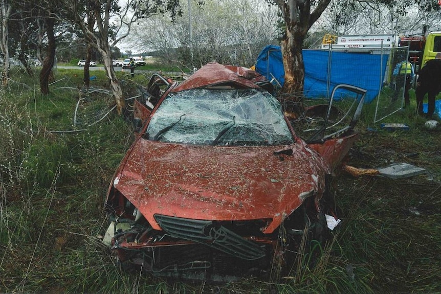 The front of a crashed red Toyota Camry, with significant damage over the whole car.