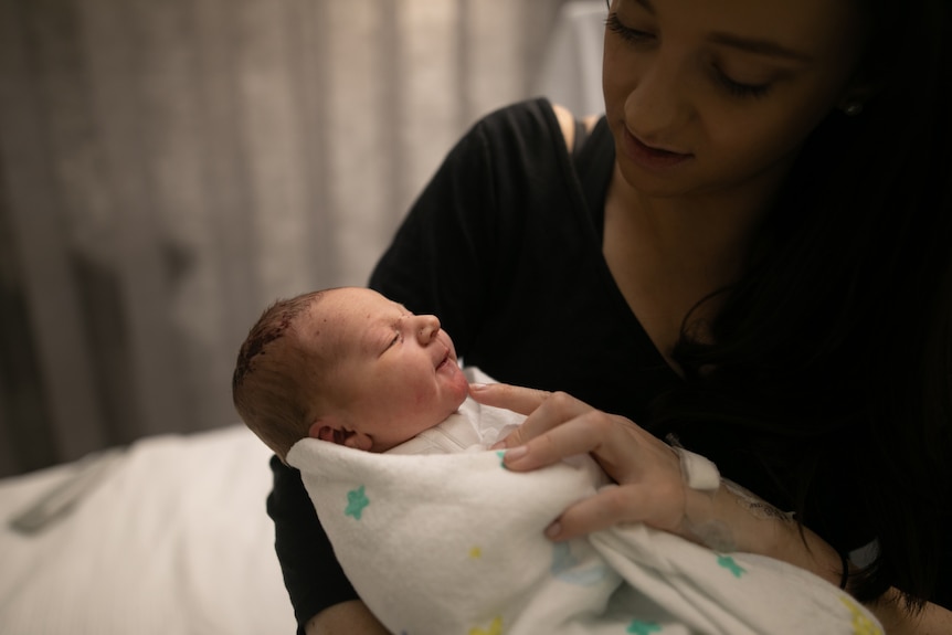 Taryn looks dotingly at her newborn baby Darci, who is wrapped up like a burrito with a little smile on her face.
