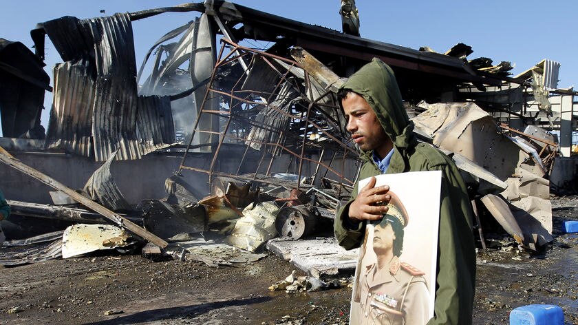 A Libyan man holds a portrait of Moamar Gaddafi at a naval facility damaged by coalition air strikes.