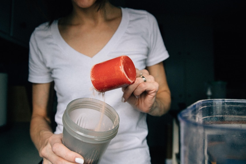 A woman shakes some powder into a protein drink.