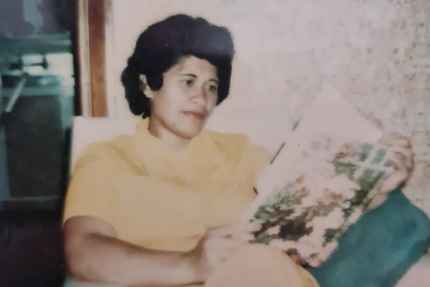 Faded photograph of a beautiful Samoan woman reading a magazine on an armchair in a yellow collared dress