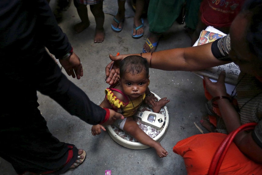 A health worker weighs a child under a government program in New Delhi.