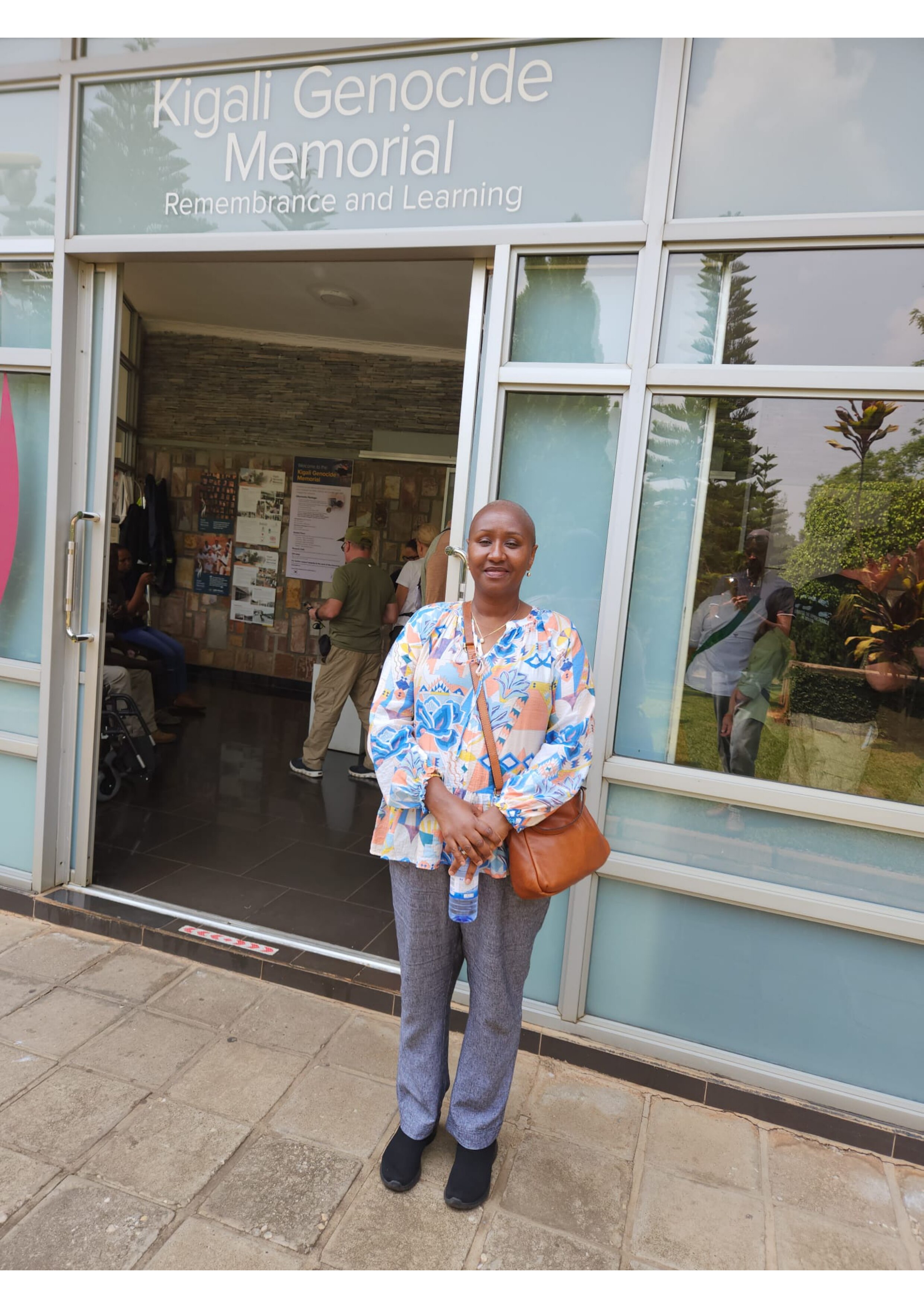 Woman stands in front of building that reads "Kigali Genocide Memorial" on outside of building