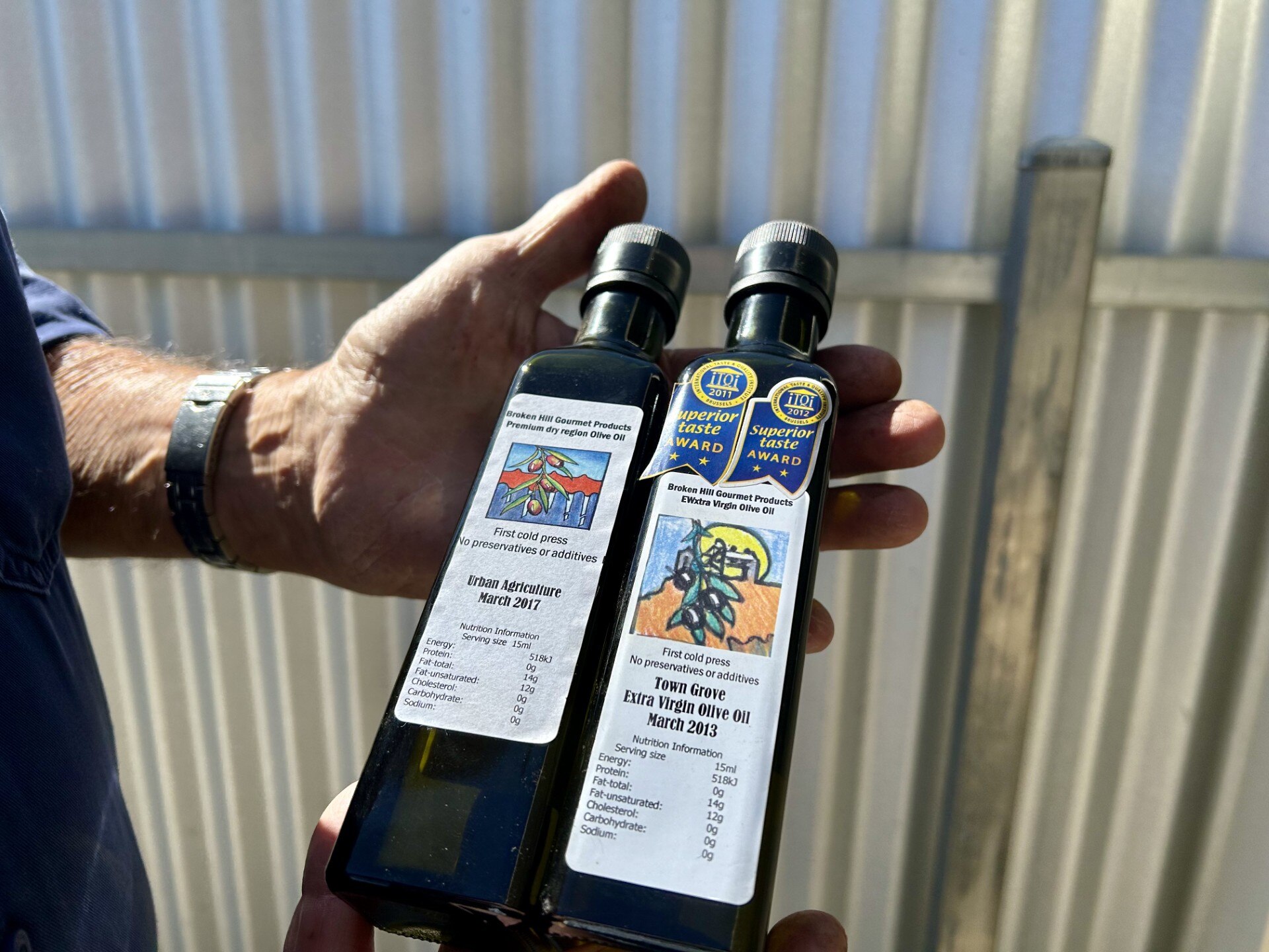 Two bottles of olive oil held in a hand.