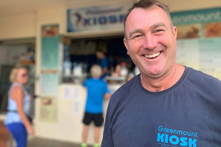 A man smiling outside a beachside kiosk