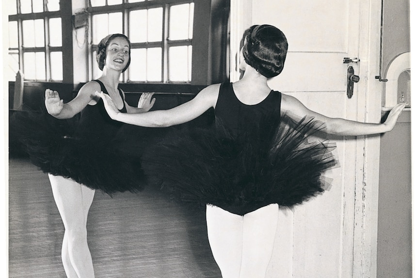 A black and white image of a teenage ballerina looking in mirror wearing tutu