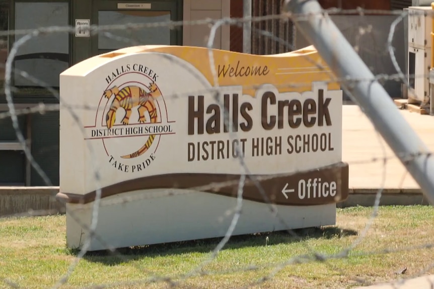 Barbed wire surrounds a sign displaying Halls Creek District High School