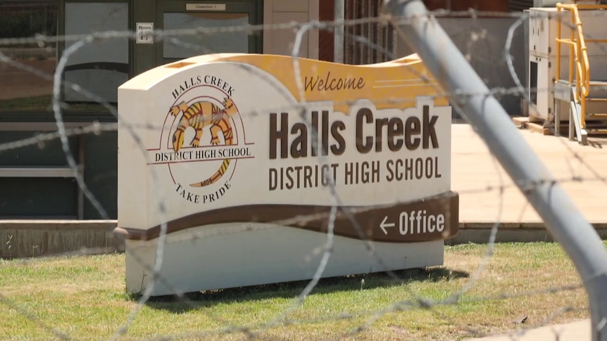 Barbed wire surrounds a sign displaying Halls Creek District High School